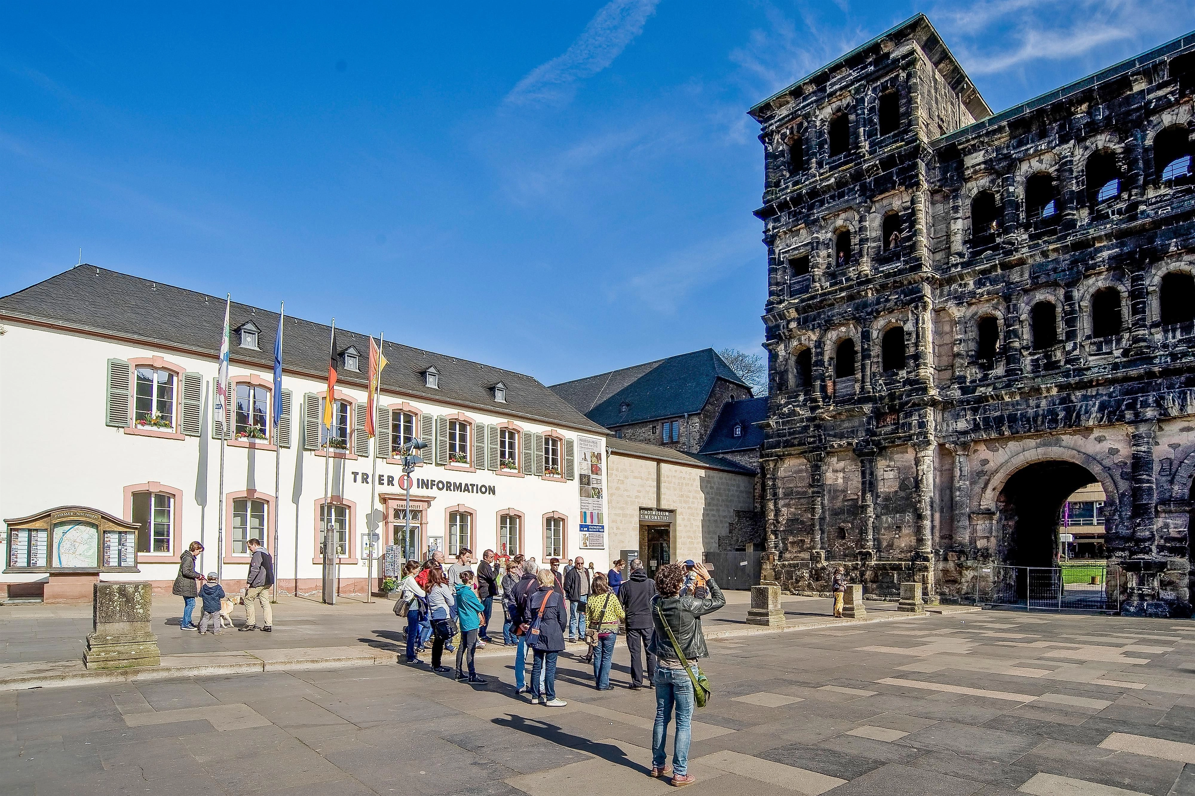 Ein historisches Gebäude mit zerfallener Fassade steht neben einem Informationszentrum. Touristen besichtigen die Sehenswürdigkeit bei klarem Himmel.